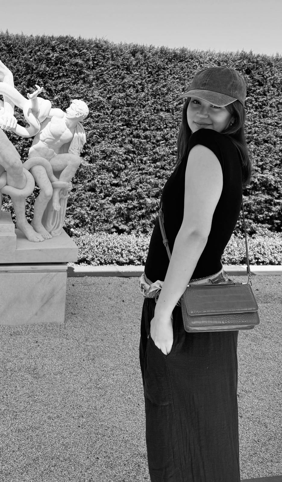 Azra Vardar outdoors beside classical sculpture.