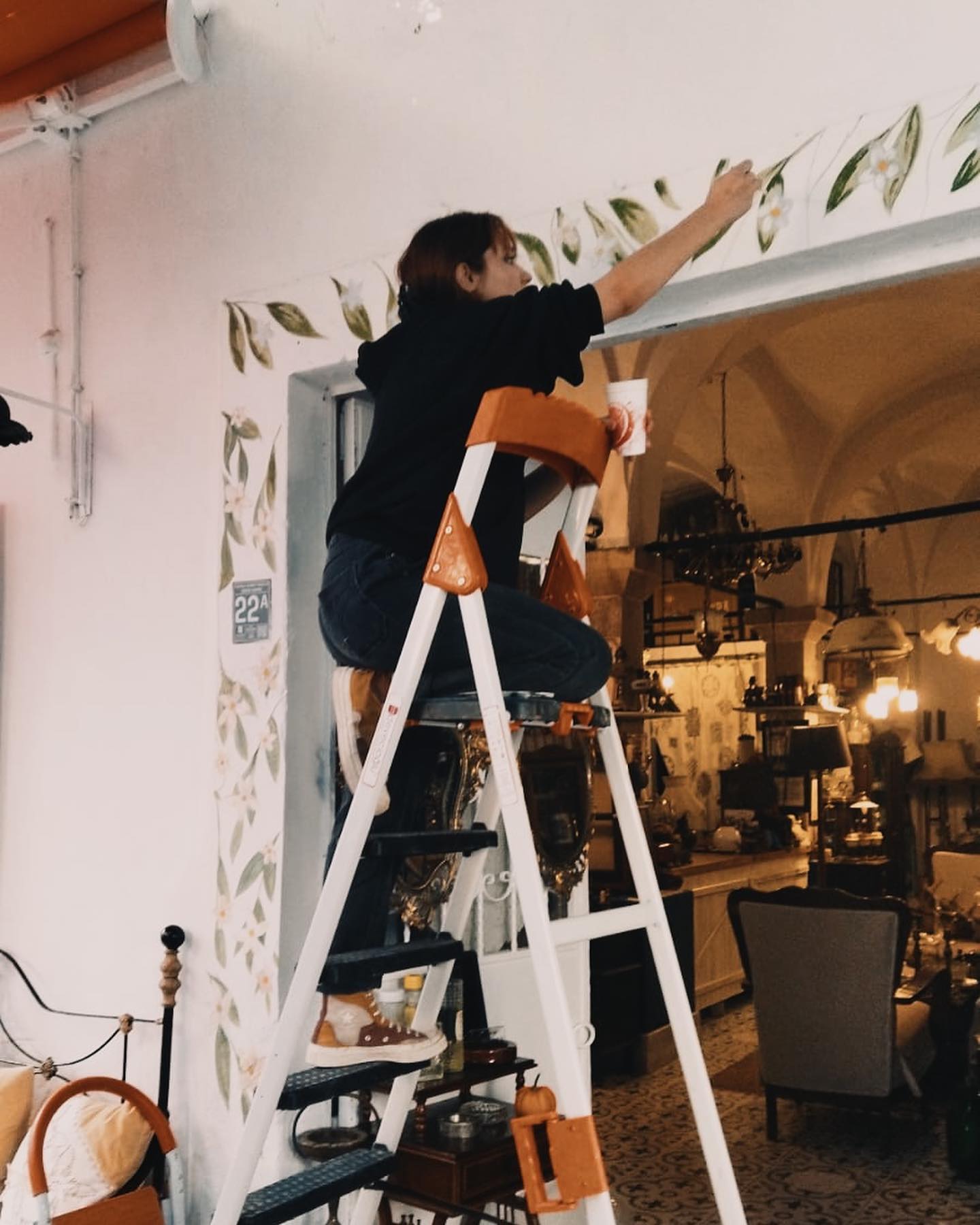 Azra Vardar painting a leafy mural around a doorway.